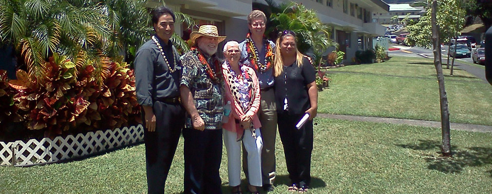 Photograph of three men and two women in casual dress standing in the lawn in front of a two-story residential building.