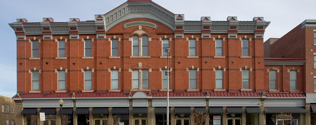 Photograph of a three-story mixed-use building with storefronts lining the first floor. 