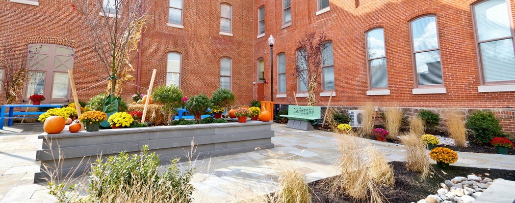 Photograph of a landscaped patio, contained on two sides by a three-story building. 