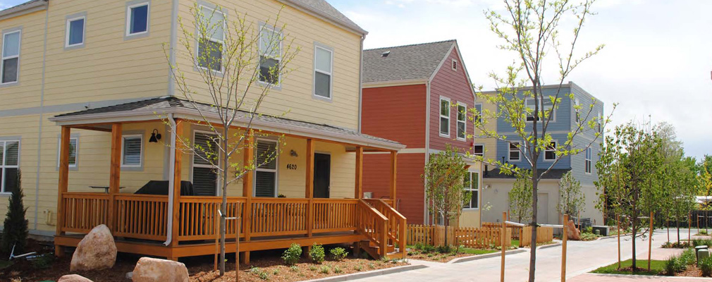 Photograph showing a 2-story single-family detached home with a front porch, with other residences in the background, on the narrow lane. 