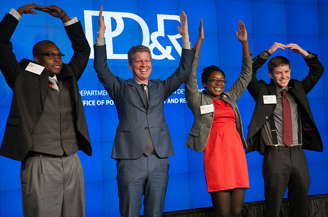 Four individuals, including three members of the Ohio State University team and HUD Secretary Shaun Donovan (second from left), pose in front of a backdrop with a PD&R logo, using their arms to spell out the word “Ohio.”