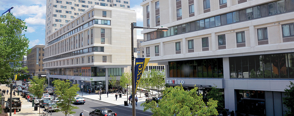 Photograph of two 8-story buildings with commercial space on the ground floor and residences on the upper floors. A residential tower of approximately 20 stories is attached to one of the mixed-use buildings.