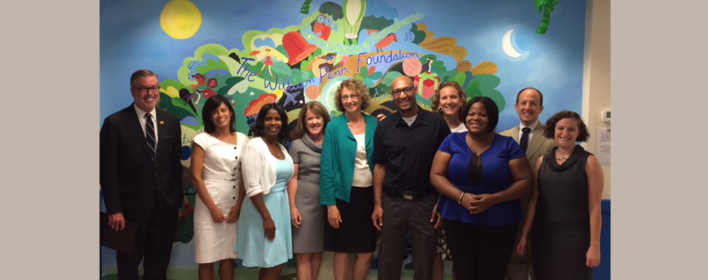 Photograph of 10 people posed in front of a mural with the words “The William Penn Foundation.”