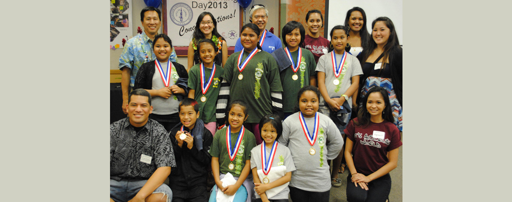 Photograph of faculty and students, some wearing gold medals, in a school classroom. 