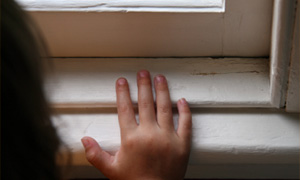 An image of a child’s hand on a window sill with peeling paint.