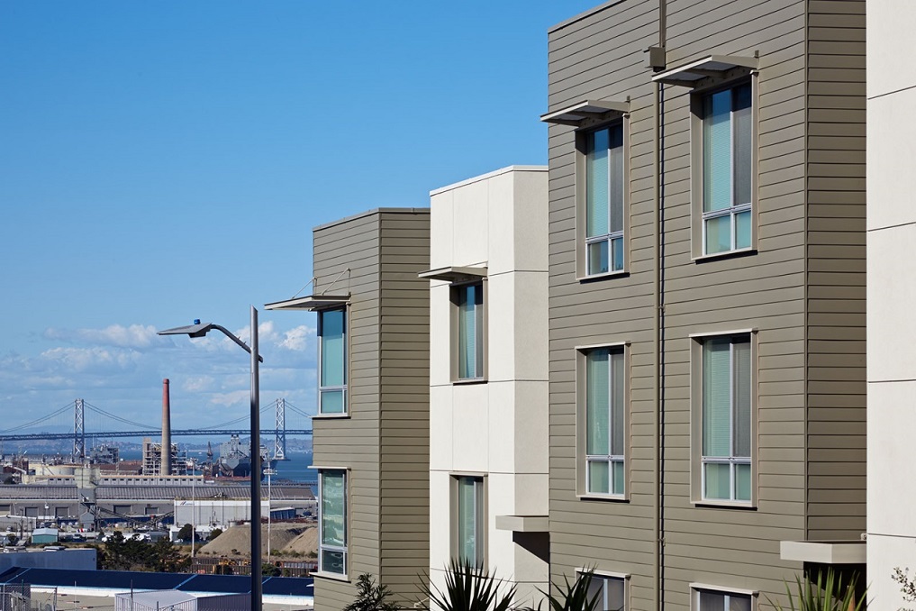 Exterior image displaying the upper floors of a multi-story residential building, with a view of the San Francisco bay in the background.