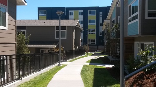 Photograph of a path between two-story houses with a multifamily building in the background