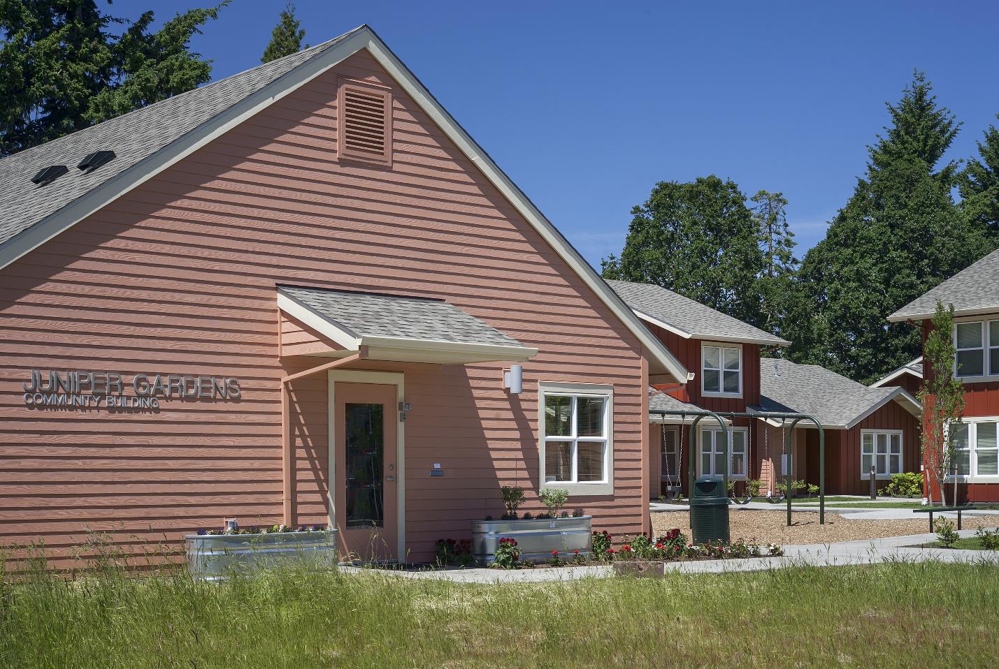 Photograph of Juniper Gardens’ one-story community building, located next to a play area with swings for children.