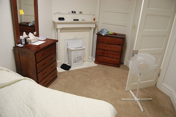 Photograph of a carpeted bedroom furnished with a bed and two dressers.