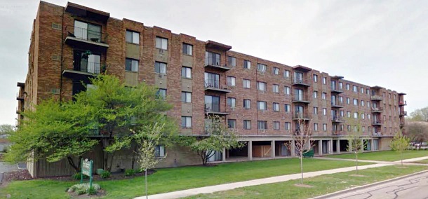 Exterior image of a 5-story, brick residential building. A road, sidewalks, and vegetation are visible in the foreground.