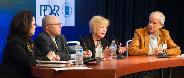 Image showing four individuals, including Director of HUD’s Office of Economic Resilience Harriet Tregoning and three panelists, seated at a table bearing the HUD logo. An image with the HUD and PD&R logos is visible on a screen behind the table. 