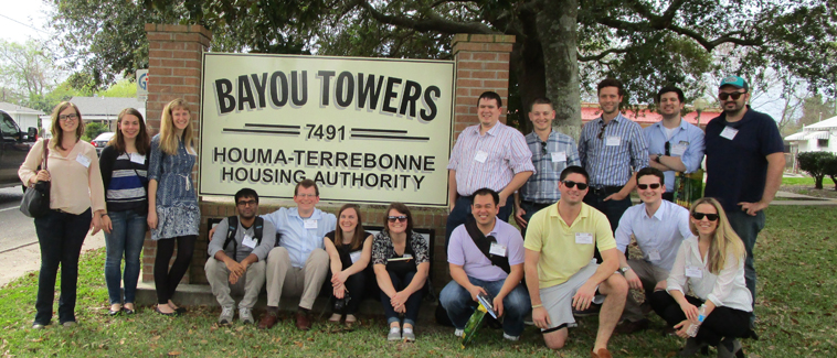 Photograph of 16 students surrounding around a large sign marking the Bayou Towers property.