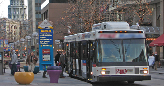 Image of passengers boarding an RTD bus at a bus stop in downtown Denver, surrounded by tall buildings.