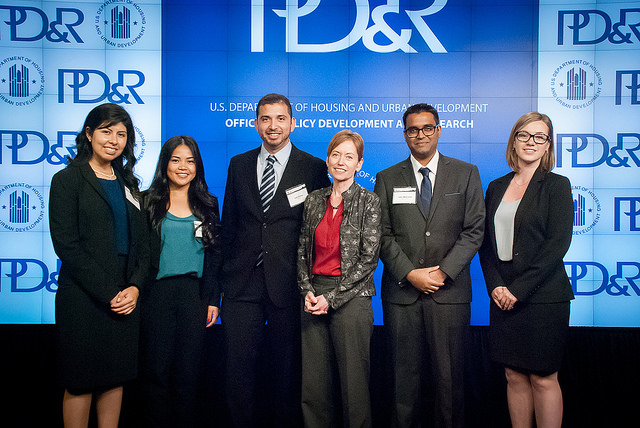 Photograph of five students from the University of California, Los Angeles graduate student team and Assistant Secretary for Policy Development and Research Katherine O’Regan (third from the right), posing on stage in front of a PD&R banner.