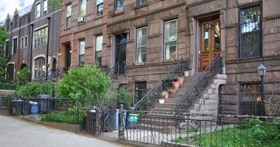 Exterior image of Brooklyn brownstone townhomes with gated entrances from the sidewalk.