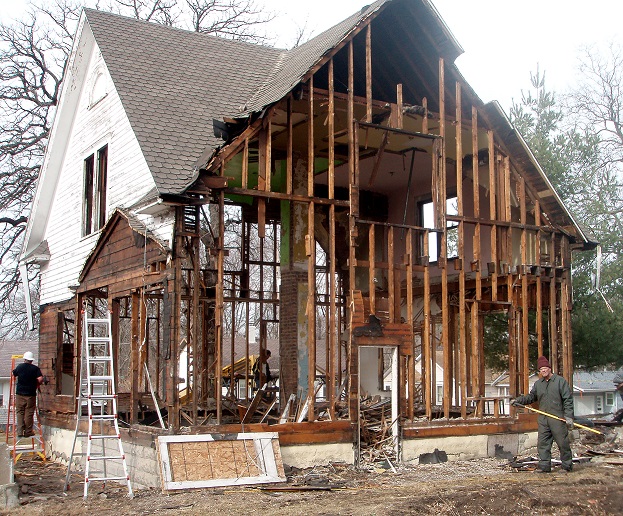 Workers deconstructing a house, which involves dismantling the structure in reverse order of its construction.
