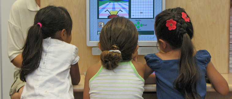 Image of three young girls looking at a computer screen at a desk.