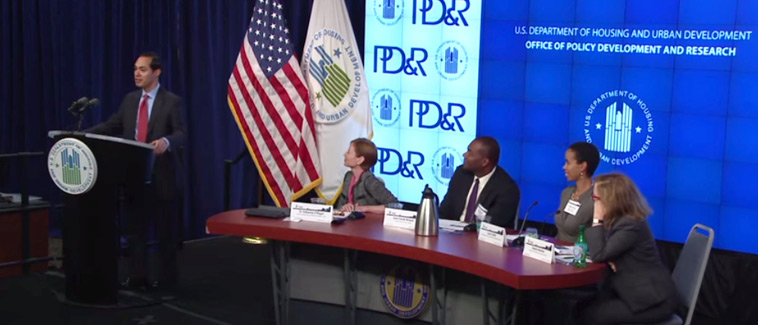 Image displaying HUD Secretary Julián Castro speaking at a podium bearing the HUD logo, with the American flag and a HUD flag behind him. To the right of the podium, a table with four seated individuals, including Assistant Secretary of PD&R Katherine O’Regan and three panelists, is visible, and a backdrop with the HUD and PD&R logos is shown in the background.