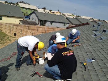 Five students in hard hats working on a roof to install a solar system.