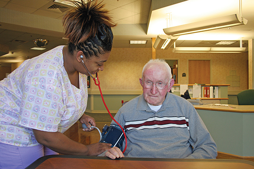 A nurse taking a blood pressure reading for an elderly man living in a nursing home.