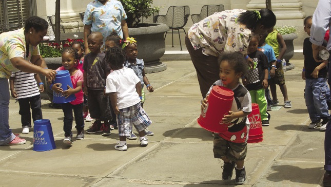 A group of preschool children with adults helping them with an organized, coordinated play activity.
