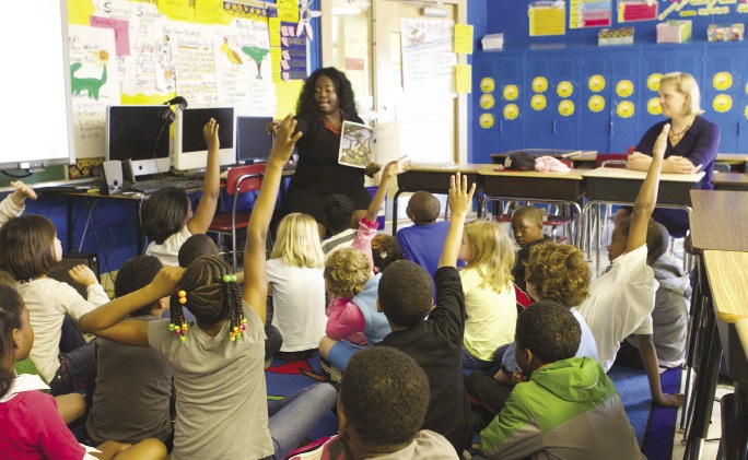 A classroom showing students excitedly interacting with a teacher.