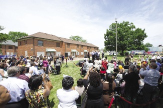 A large group of community members gathered on a lawn to commemorate the opening of a nearby mixed-income housing development.