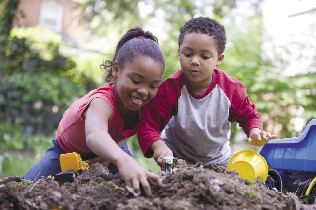  A boy and a girl digging with their hands in a pile of dirt.