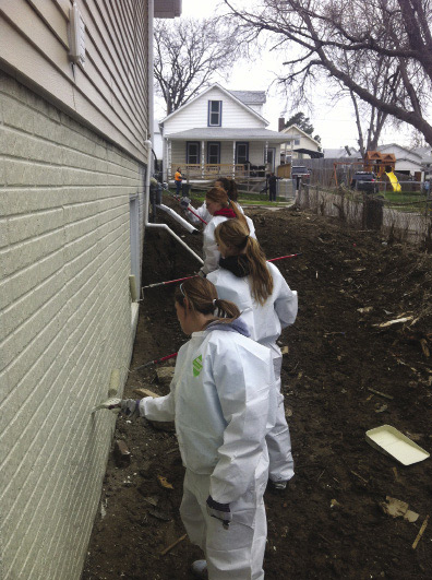  Volunteers in protective coveralls painting a house.
