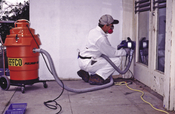A worker in protective clothing and using a special sander to minimize lead-based paint exposure.