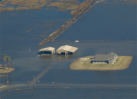 A house located on a slightly raised area is protected from flood waters.