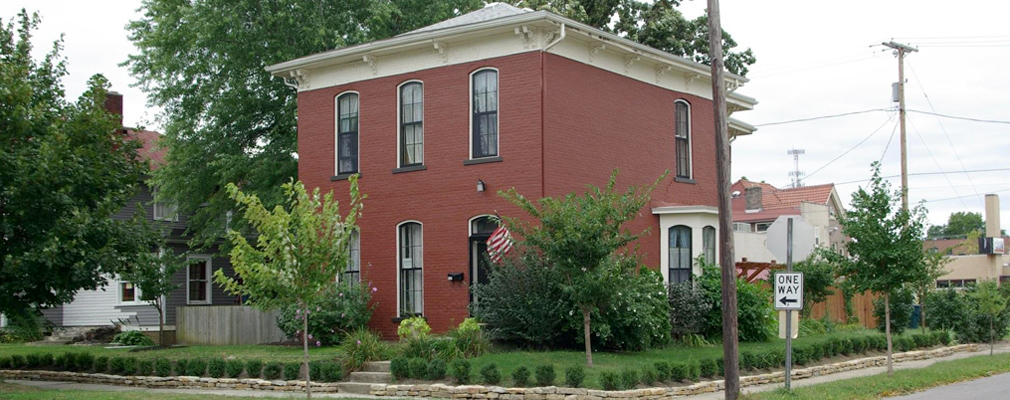 Photograph of two façades of a two-story brick house on a corner lot.