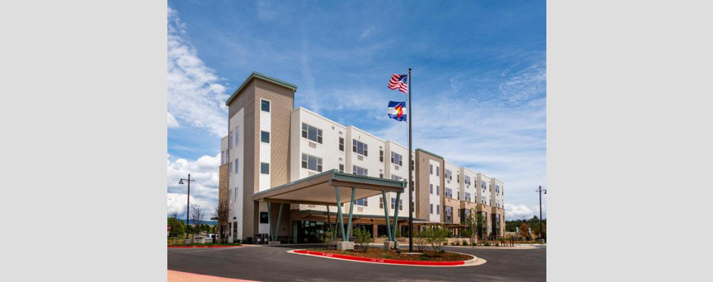 Perspective view of a four-story building with a covered entrance, roundabout and a flagpole flying the flags of the United States of America and the state of Colorado.