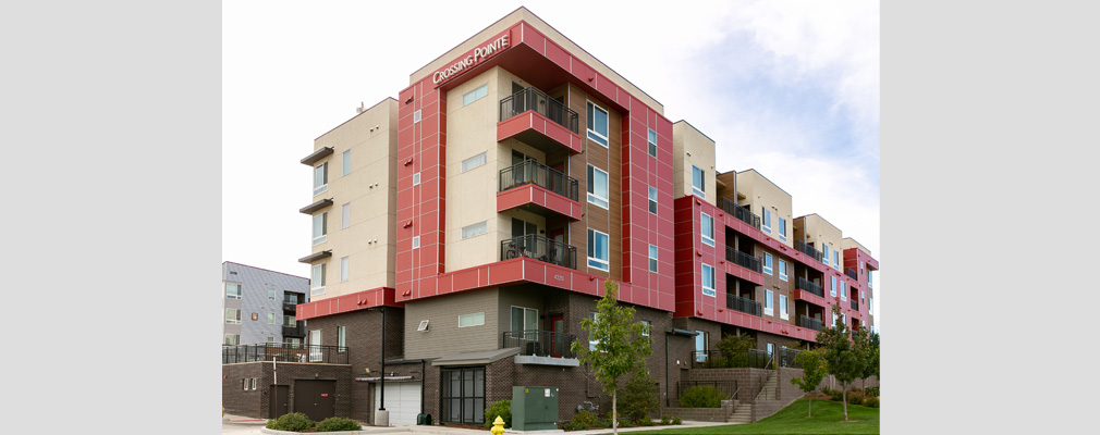 Four-story residential building with balconies on each floor and a side entrance and garage door.