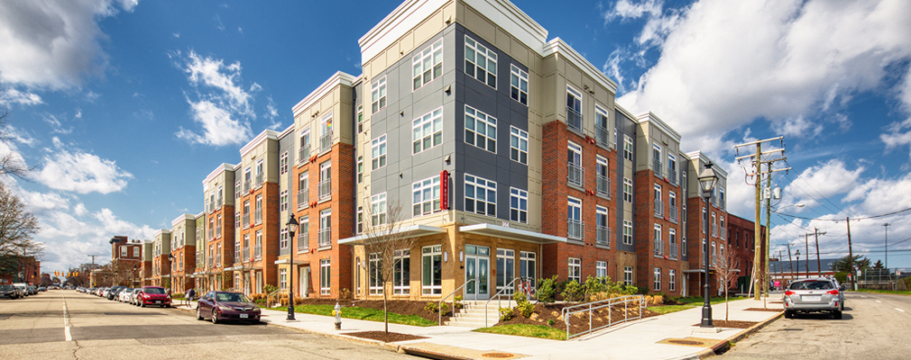 Photograph of two street façades of a four-story multifamily building.