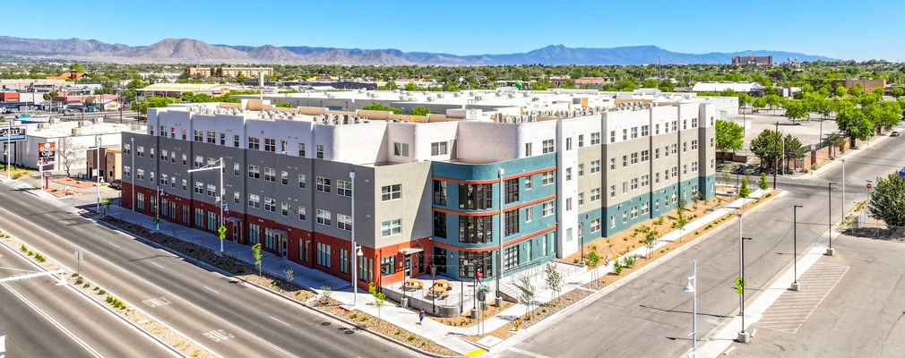 Low aerial photograph of a four-story building situated at an intersection with a mountain range in the background.