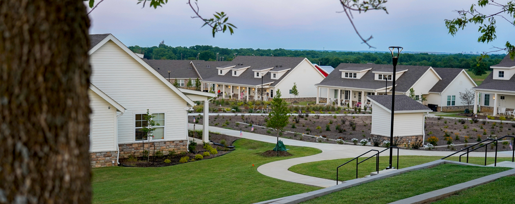 White, one-story residential buildings surrounding a large garden plot.