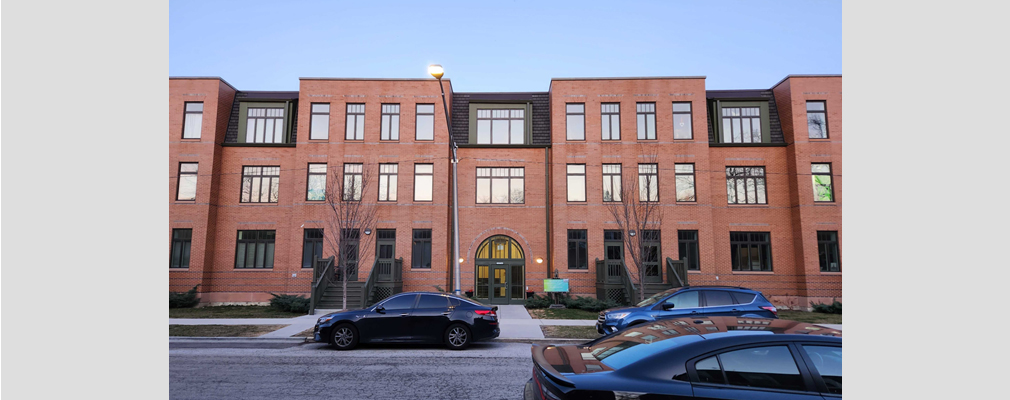 Three-story brick apartment building with cars parked in front.