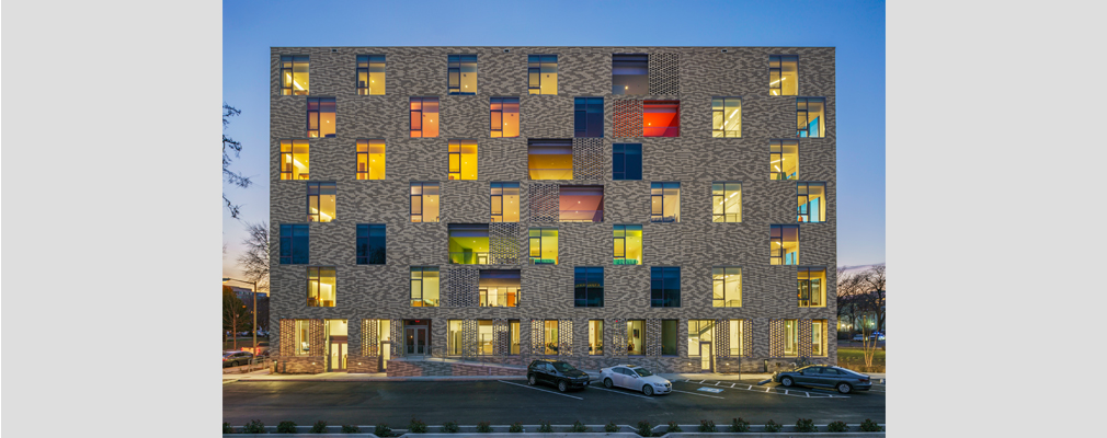 Night view of lighted seven-story residential building with cars parked in front.