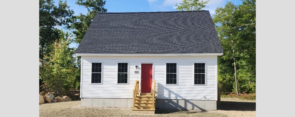 Front view of a small single-family house with white siding, a red door, and several windows. 