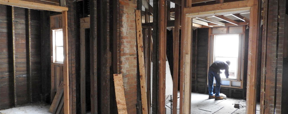 Interior photograph of a gutted house, with a worker installing a window.