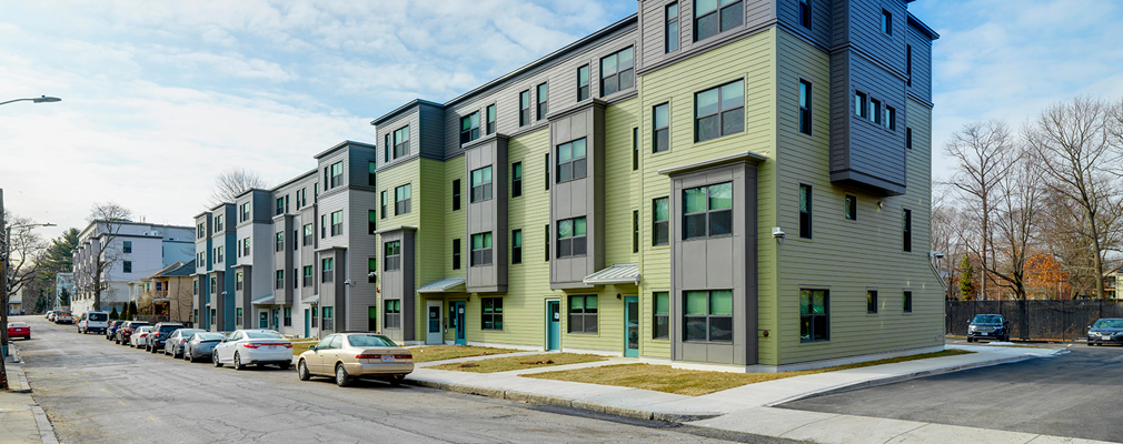 Four-story, townhome-style buildings along a street lined with parked cars.