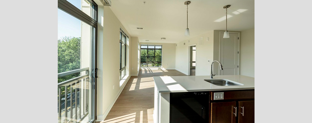 An empty apartment with large windows and vinyl plank flooring.