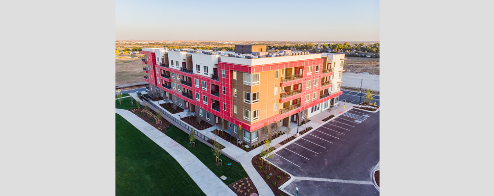 Aerial view of a four-story residential building with a lawn and sidewalk on one side and parking spaces on two sides.