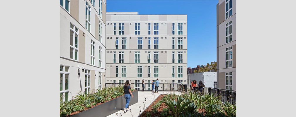 Photograph of a courtyard with plantings and ornamental fencing, framed by three five-story buildings.