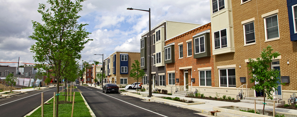 Tree lined road with multicolored two- and three- story residential buildings.