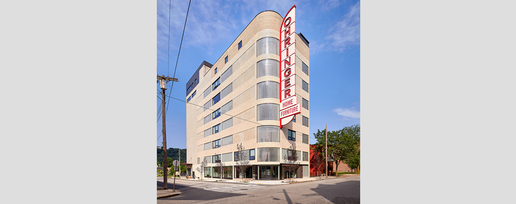 Photograph of the two street façades of the Ohringer Arts Building, an eight-story structure with a five-story blade sign that reads "Ohringer Home Furniture.”