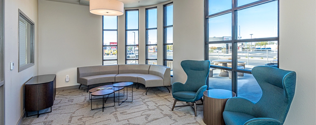 Interior photograph of a room with a curved wall, curved windows, two chairs, a curved couch, and multiple tables.