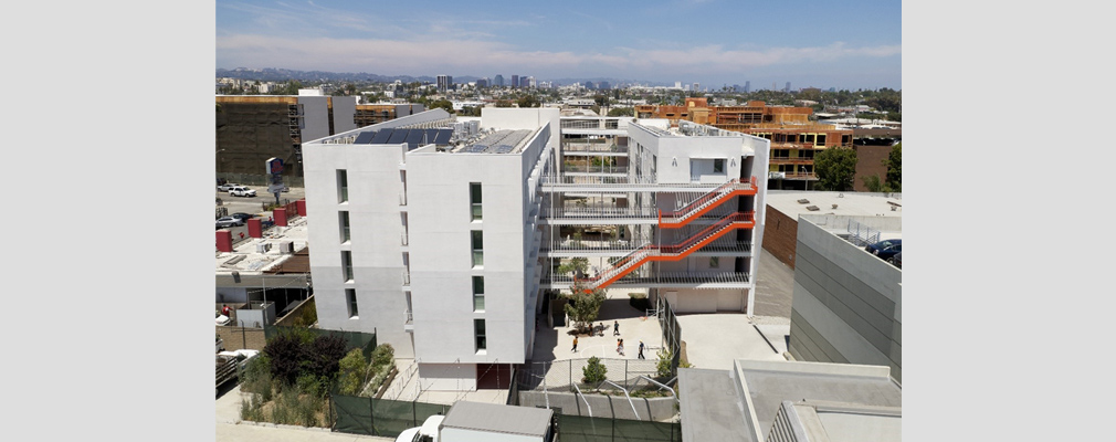 Low-angle photograph of the rear façade of a multistory residential building, with open walkways on each floor connecting the two wings of the building.