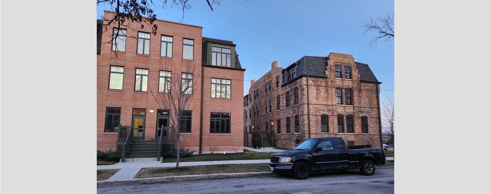 An older three-story brick building and a new three-story structure separated by a sidewalk.